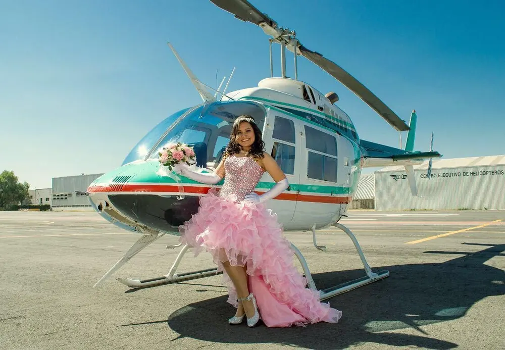 Quinceañera con vestido rosa junto a un Bell 206 en la plataforma